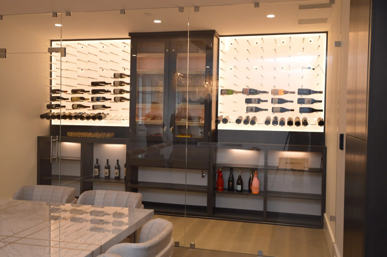 Backlit bottle displays and wood cabinetry behind a glass wine-room enclosure.