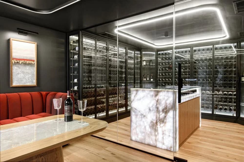 A glass wine room beside a stone tasting island and upholstered banquette.