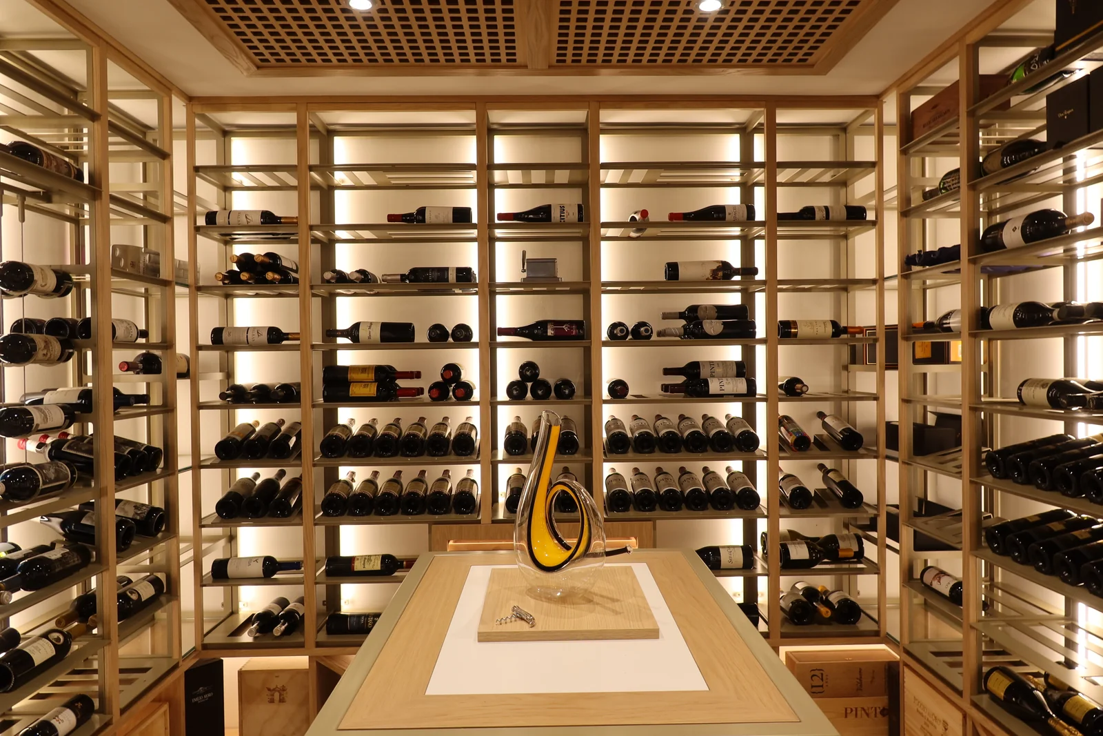 A warmly lit wine room with brass-toned shelving and a central tasting counter.
