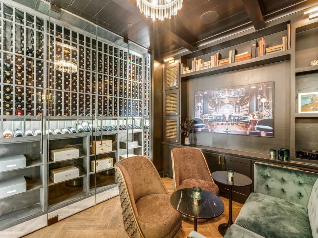 A lounge with upholstered chairs beside glass-front wine storage and display cabinetry.