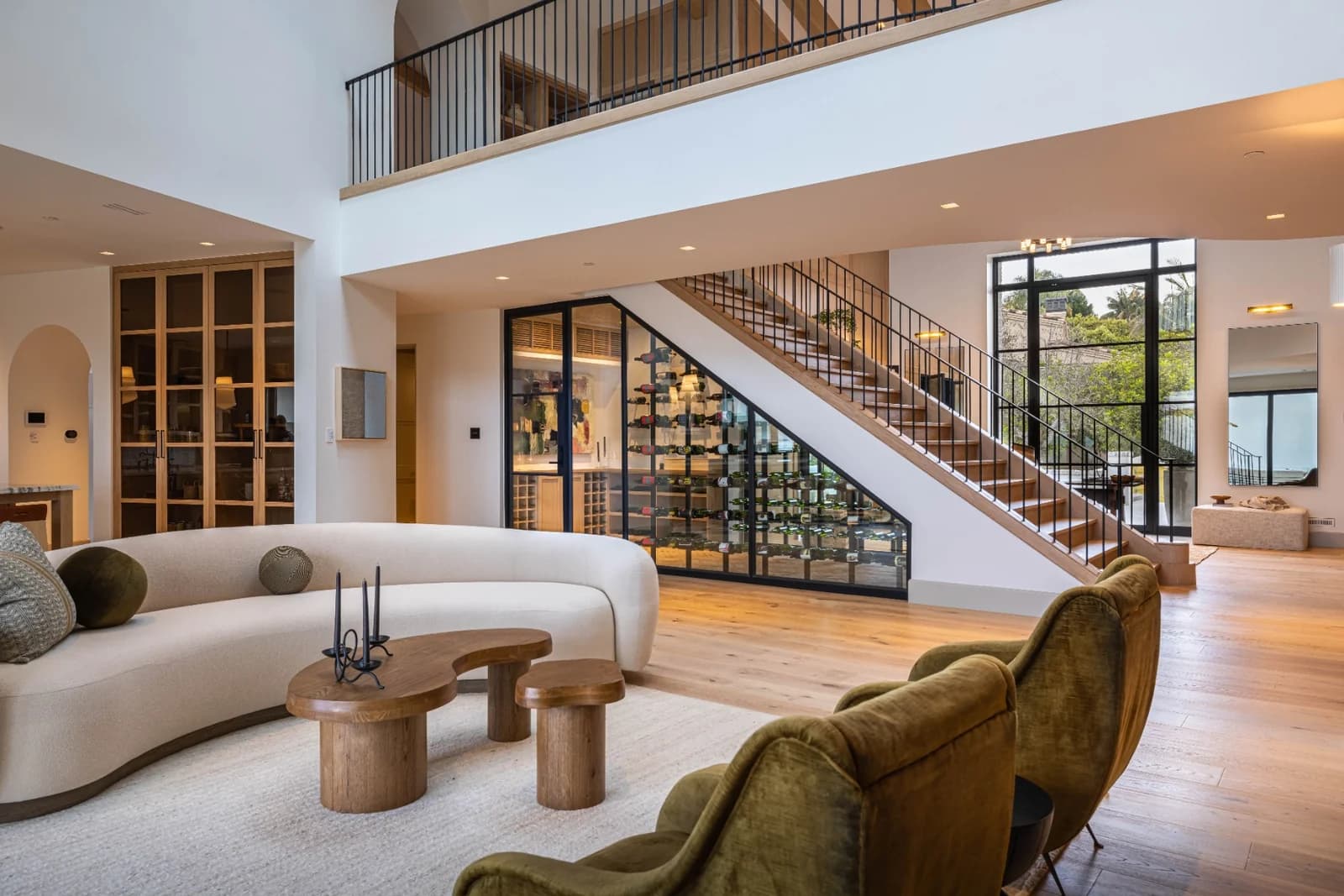 A glass-enclosed wine room beneath an open staircase in a bright living space.