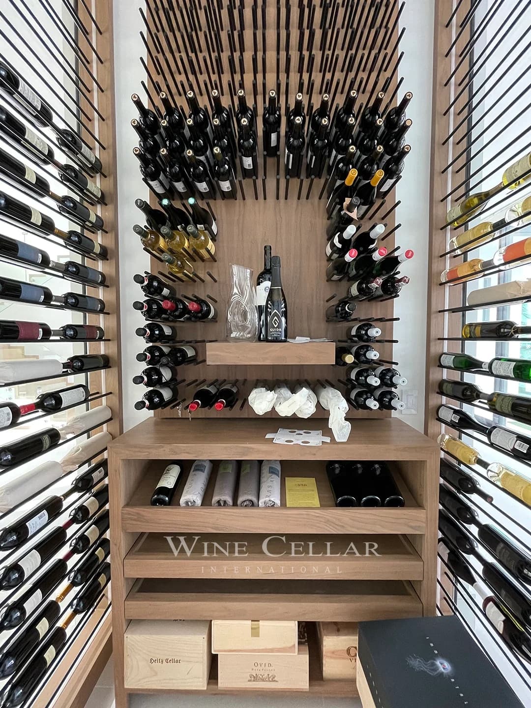 Floor-to-ceiling bottle racks and wood shelves inside a glass-enclosed wine room.
