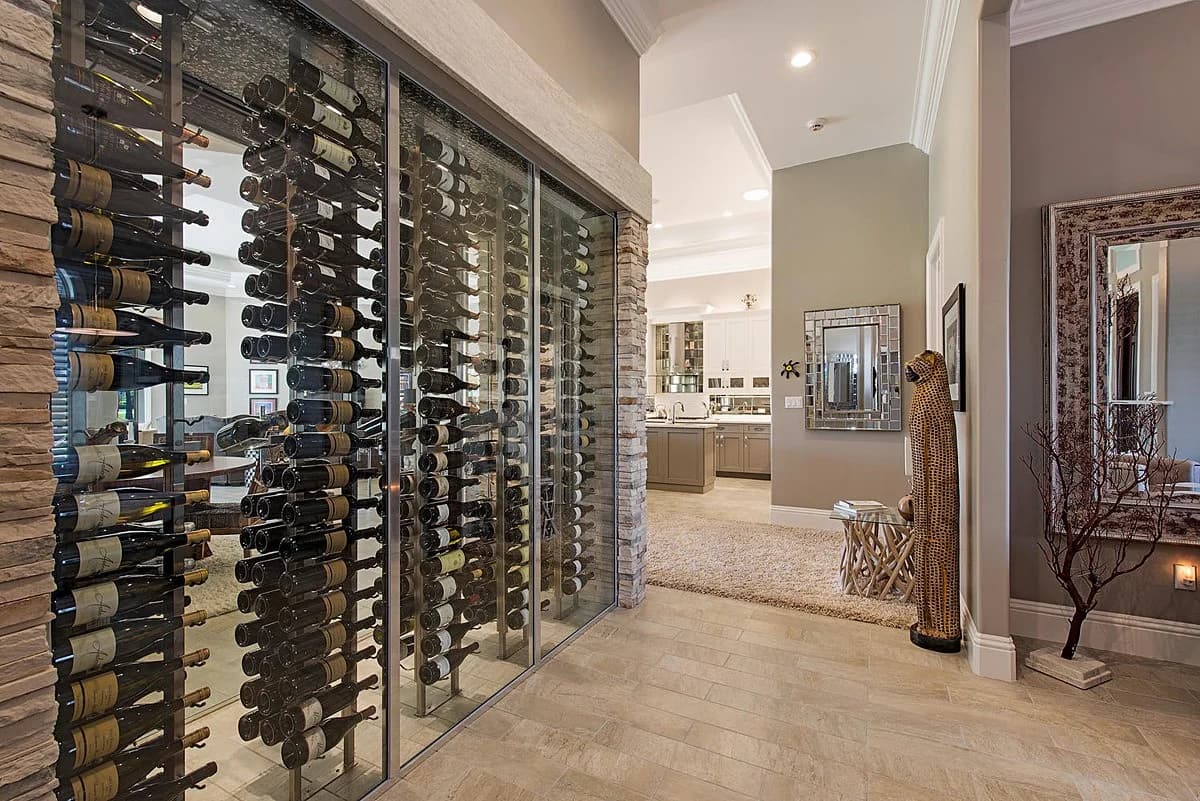 A glass-front wine room with metal bottle racks beside a bright residential hallway.